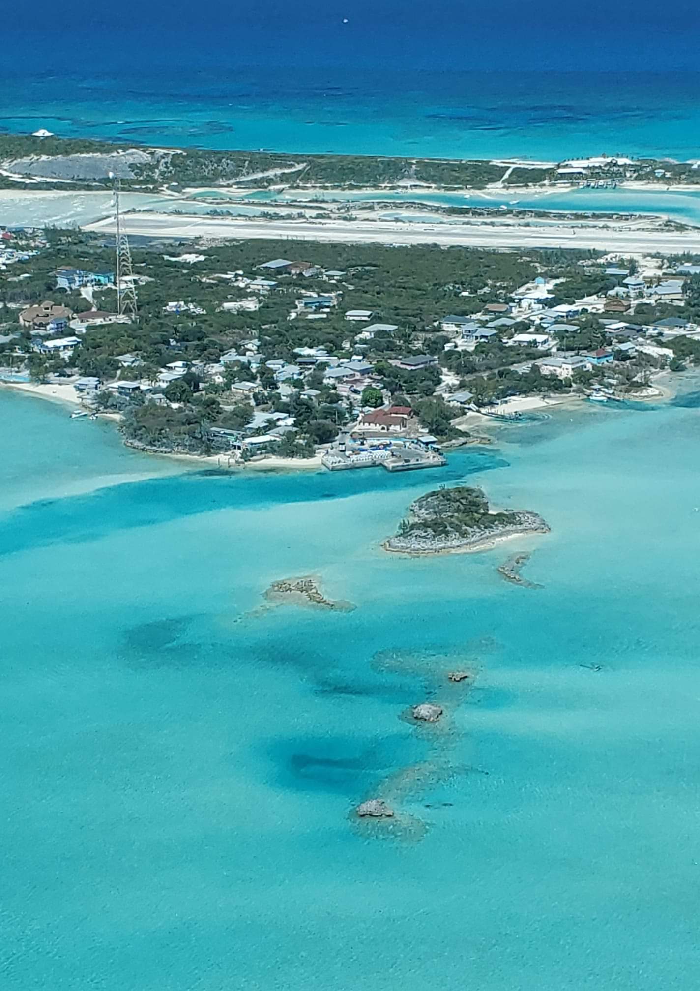 Aerial view of a coastal town surrounded by turquoise water with small islands and a distant sandy beach.