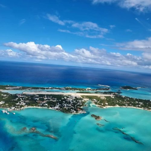 Aerial view of an island surrounded by vibrant turquoise waters, dotted with buildings and clear skies above.