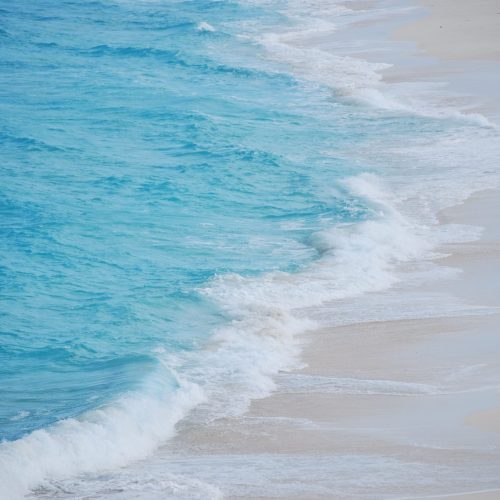 Waves gently crashing on a sandy beach with clear blue water under bright daylight.