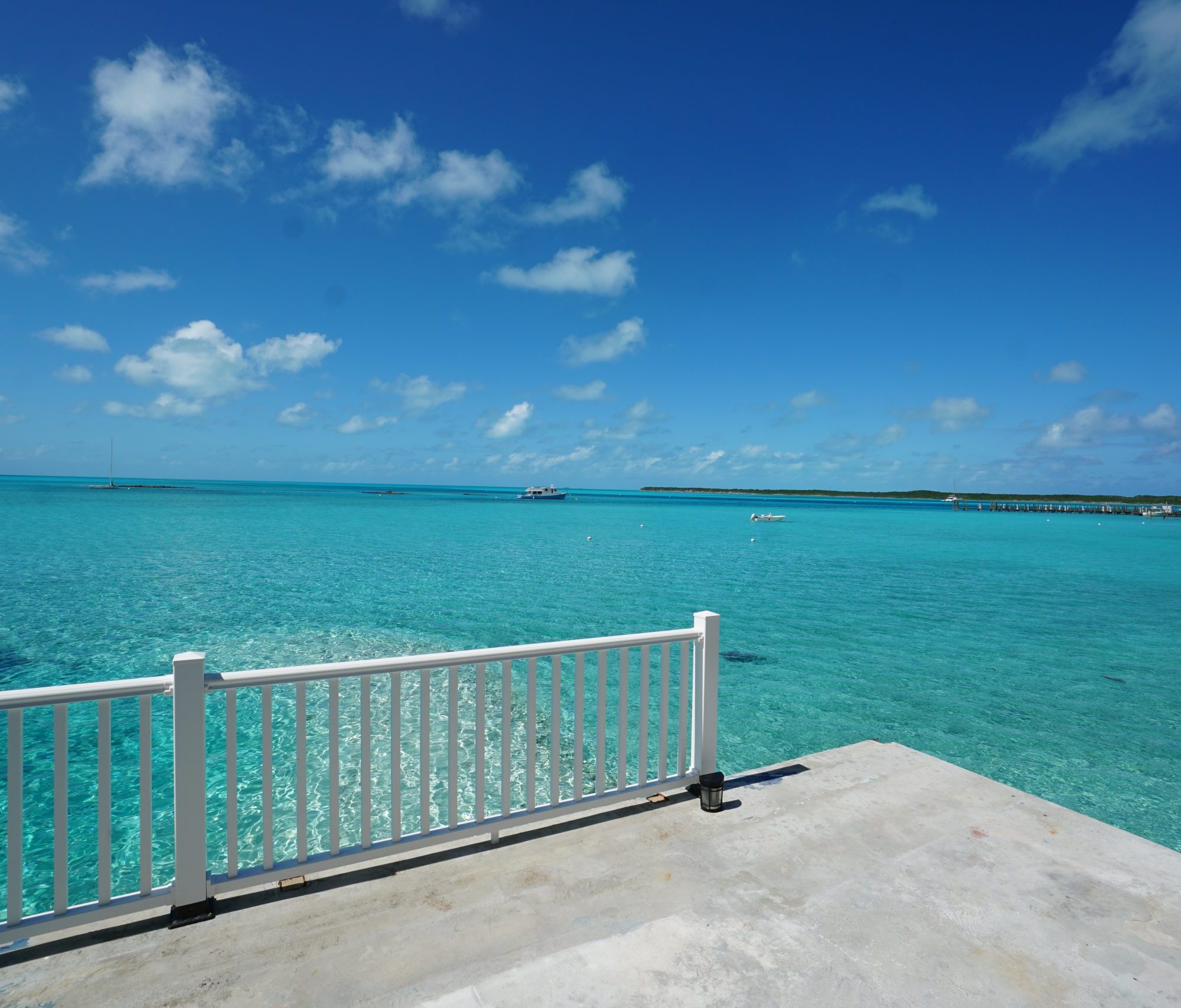 Stanie Cay Vacation rentals one bedroom apartment on the water Clear turquoise ocean with a white fence in the foreground and a blue sky with scattered clouds in the background.