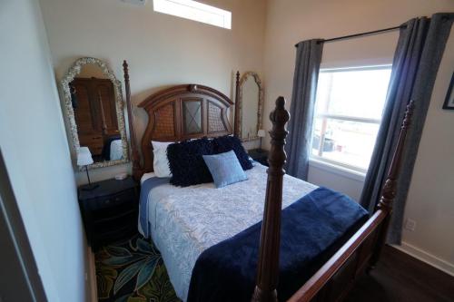 Staniel Cay Vacation Rentals, One bedroom on the water with view of the Staniel Cay Yacht Club.A small bedroom with a wooden four-poster bed, two mirrors on either side, a nightstand with a lamp, and a window with curtains. The bed is adorned with blue and white bedding.