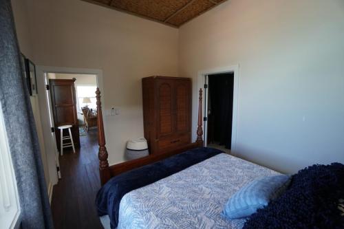 A bedroom with a four-poster bed, blue and white bedding, and a wooden wardrobe. A doorway leads to an adjacent room with visible furniture.