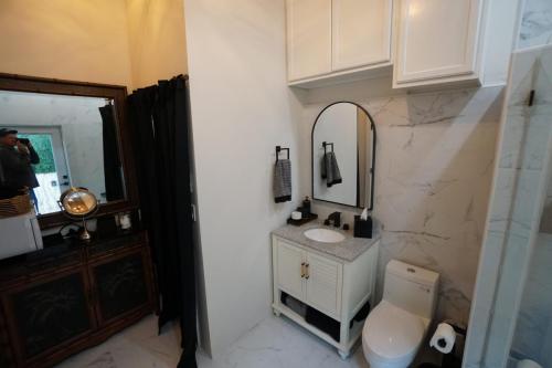 Bathroom with a white vanity, mirror, marble walls, and towel racks. A wooden cabinet with a round mirror is on the left.