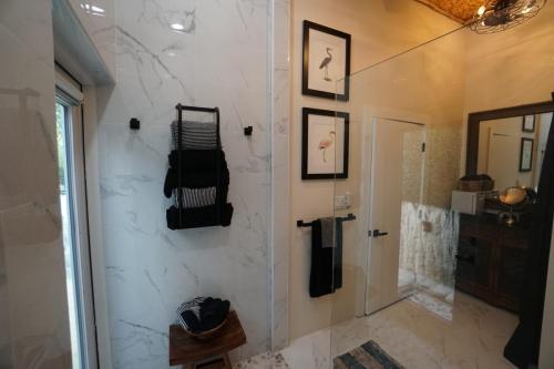 Modern bathroom with white marble walls, glass shower door, towel rack, framed bird art, and a wooden stool. Staniel Cay Vacation Rentals, One bedroom on the water with view of the Staniel Cay Yacht Club.