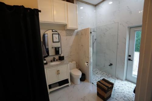 Modern bathroom with white cabinets, a round mirror above a sink, a toilet, and a glass-enclosed shower. Gray marble walls and floor tiles complement the decor. A woven basket is on the floor.