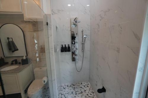 Staniel Cay Vacation Rentals, One bedroom on the water with view of the Staniel Cay Yacht Club. A modern bathroom with a glass-enclosed shower, marble tiles, rainfall showerhead, built-in shelving, and pebble floor. A vanity with an oval mirror and a toilet are visible on the left.