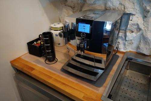 A large coffee machine with a digital display is placed on a wooden counter, next to a milk frother and a black container with miscellaneous items.