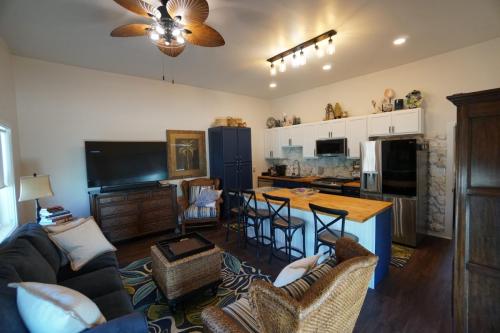 A cozy living area with wicker chairs, a sofa, large TV, and a kitchen featuring a wooden island and modern appliances.  Staniel Cay Vacation Rentals, One bedroom on the water with view of the Staniel Cay Yacht Club.Ceiling fan and warm lighting create a comfortable atmosphere.