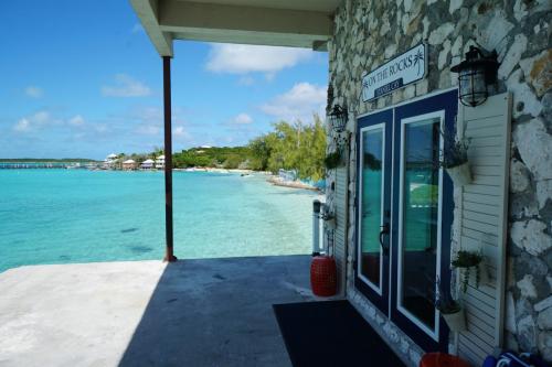 A stone building with a sign On the Rocks overlooks a clear turquoise sea, under a partly cloudy blue sky. Staniel Cay Vacation Rentals, One bedroom on the water with view of the Staniel Cay Yacht Club.