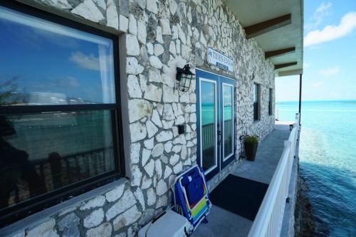 Vacation On Staniel Cay, BahamasA stone-clad building with a glass door overlooks a clear turquoise ocean. There is a colorful folding chair leaning against the wall beside the door.