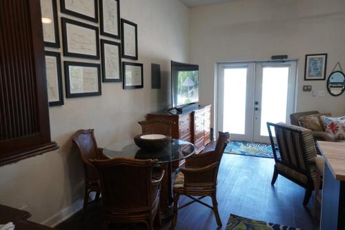 A living room with a round glass dining table and chairs, a TV on a wooden stand, a couch, and framed pictures on the walls.