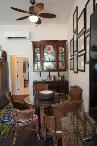 A kitchen with a round glass table, wicker chairs, a ceiling fan, wall art, and a wooden cabinet displaying dishes. A doorway is visible in the background.