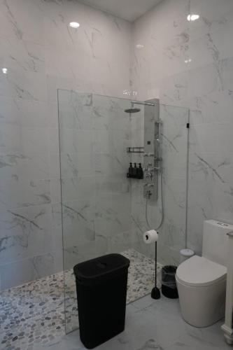 Modern bathroom with marble tiles, a glass shower enclosure with rain showerhead, a black laundry basket, and a white toilet with nearby toilet paper holder.