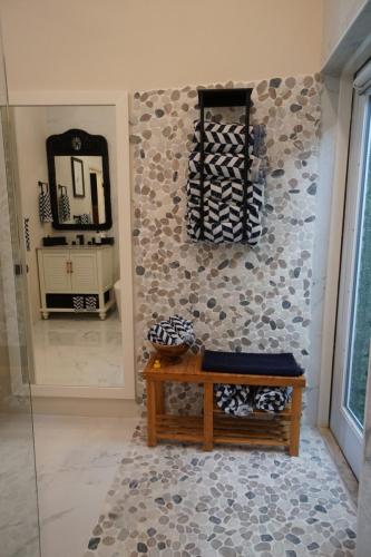 Vacation Rentals On Staniel Cay, BahamasBathroom with pebble tile accent, wooden bench with towels, and a wall-mounted towel holder. Large mirror reflects vanity with sink.