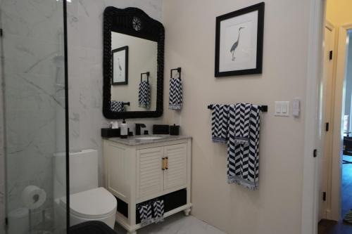 Bathroom with a black-framed mirror, white vanity, and patterned towels. A framed bird artwork is on the wall, and a glass shower is partially visible.