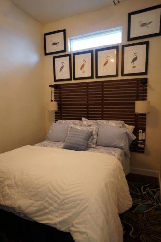 Vacation Rentals On Staniel Cay, Bahamas A cozy bedroom with a bed covered in white linens, blue pillows, and wooden headboard. Bird-themed artwork is hung above on the wall.