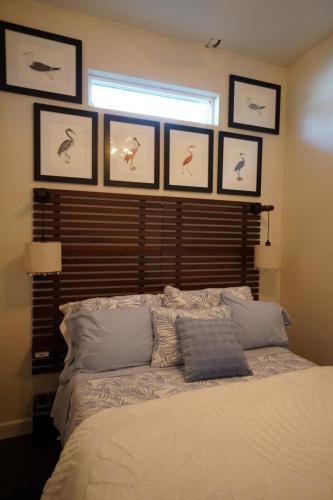 A cozy bedroom with a bed featuring blue and white bedding. Above, six framed bird illustrations hang on the wall. Two lamps are mounted on the headboard.