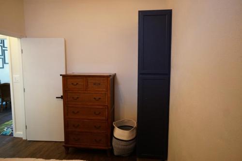 Room corner with a wooden dresser, a tall blue wardrobe, an open door, and a woven basket on the floor.