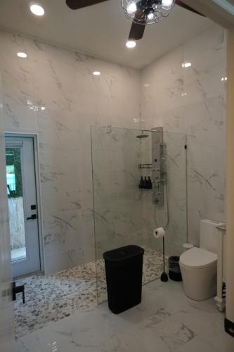 A modern bathroom with marble tiles, a glass-enclosed shower, a toilet, a ceiling fan, and a trash bin.