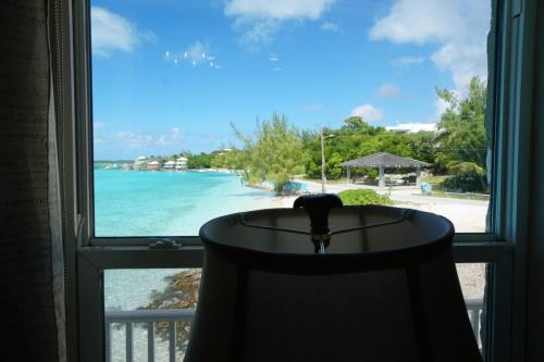 View through a window of a tropical beach with turquoise water, shoreline buildings, and a gazebo. A lampshade is in silhouette in front of the window.