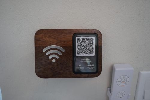 A wooden Wi-Fi sign with a QR code on a screen is mounted on a wall. A remote control is visible below the sign.