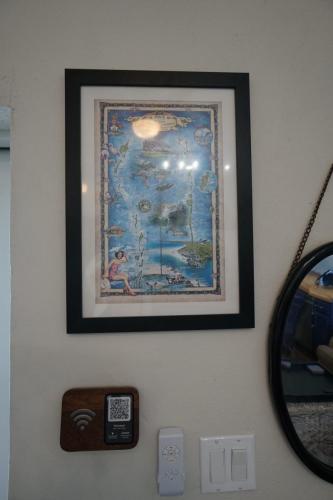 Framed colorful map illustration on a wall with a round mirror, Wi-Fi sign, and light switches beneath it.