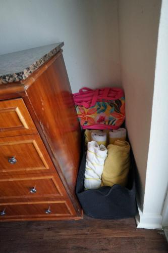 Corner with a wooden cabinet, a colorful tote bag on top, and a black basket with folded towels beside it.