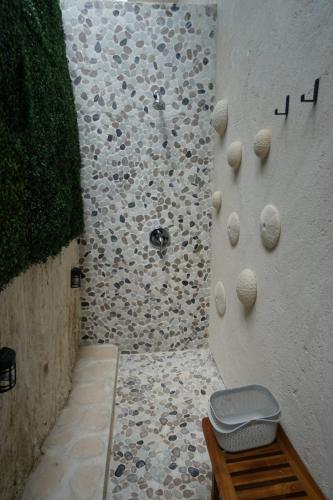 Outdoor shower with pebble stone walls, a bench, and greenery on one side. Hooks and decor adorn the wall. A wooden stool holds a basket.