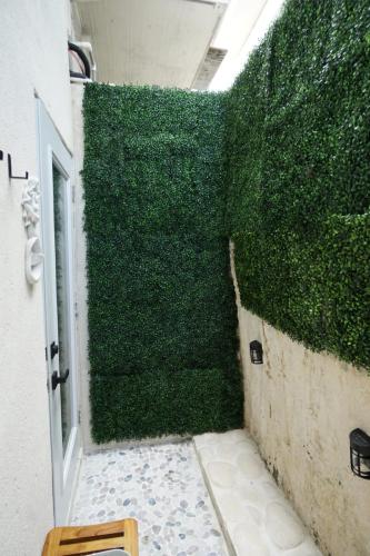 Small outdoor space with green artificial hedge walls, white stone pathway, pebble floor, and a wooden stool.