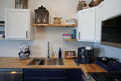 A kitchen with a wooden countertop, dual sink, espresso machine, books, and decorative items on shelves, and a gas stove.