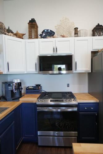 A modern kitchen featuring a stainless steel stove, wooden countertops, blue lower cabinets, white upper cabinets, and decorative items on top of the cabinets.