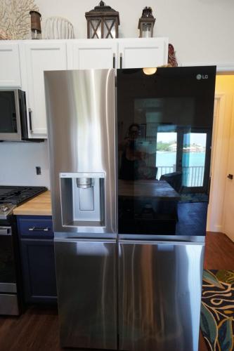 A modern stainless steel refrigerator with a sleek, mirrored right door and an ice/water dispenser on the left, situated in a kitchen with a waterfront view.