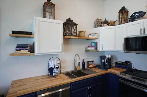 A kitchen with white cabinets, wooden countertops, a sink, a stove, and shelves holding books and decorative items.