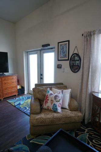 Vacation On Staniel Cay, BahamasA cozy living room corner with an armchair, decorative pillows, a wall mirror, artwork, and a TV in the background. Double doors lead outside.