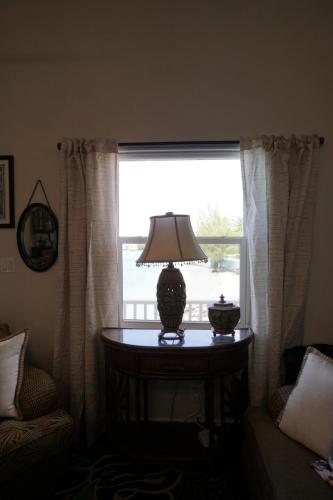 Vacation Rentals On Staniel Cay, BahamasA window with light curtains, a table with a decorative lamp, and a small pot, flanked by armchairs, overlooks a body of water.