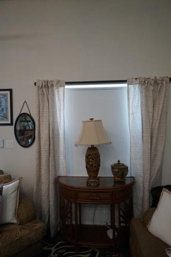 A table with a decorative lamp and bowl stands between two armchairs. Curtains frame the window behind, and a round mirror hangs on the wall.