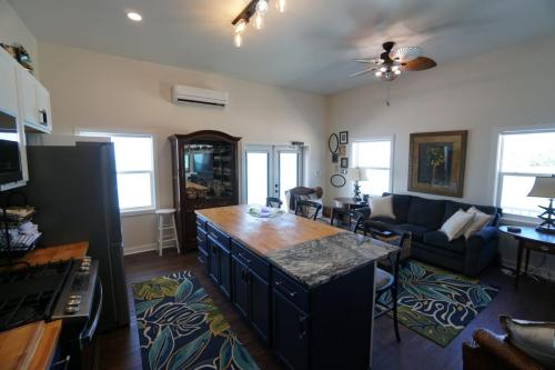 Staniel Cay Vacation Rentals, One bedroom on the water with view of the Staniel Cay Yacht Club. A modern open-concept kitchen and living area with dark countertops, a ceiling fan, framed wall art, and a blue sofa.