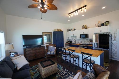 Staniel Cay Vacation Rentals, One bedroom on the water with view of the Staniel Cay Yacht Club. A cozy open-concept living room and kitchen with wooden and blue cabinetry, a ceiling fan, sofa, large TV, and a kitchen island with bar stools.