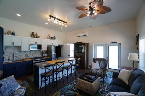 Staniel Cay Vacation Rentals, One bedroom on the water with view of the Staniel Cay Yacht Club. Coastal themed living room and kitchen with island seating, blue and white cabinets, ceiling fan, and decorative plants.